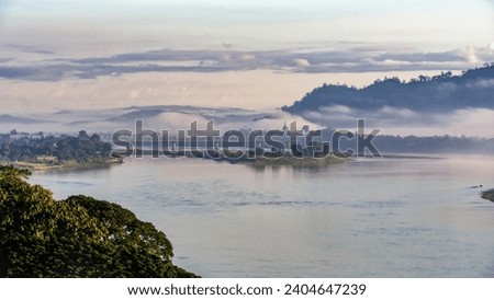 The serene morning haze settles over the Irrawaddy River, framing the Bala Min Htin Bridge in Myitkyina, Myanmar, a blend of nature's tranquility and human ingenuity