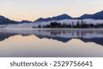 A serene morning view with mist floating over a calm lake in Mission, BC, Canada, reflecting the surrounding mountains. Peaceful and tranquil atmosphere captured at dawn.