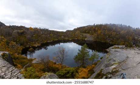 A serene mountain lake surrounded by rocky terrain and autumn foliage under a cloudy sky. - Powered by Shutterstock