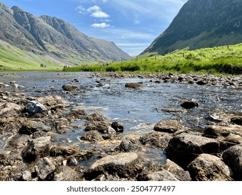 Serene mountain valley with a shallow stream flowing over rocky terrain under a bright blue sky. A peaceful natural landscape capturing the beauty of the outdoors. - Powered by Shutterstock