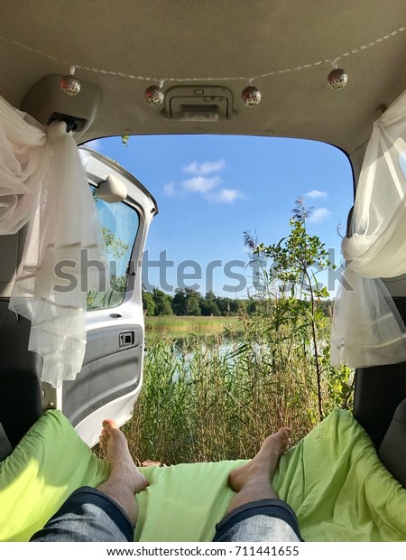 A serene nature view from a car turned camper\
with man\'s feet in the\
foreground