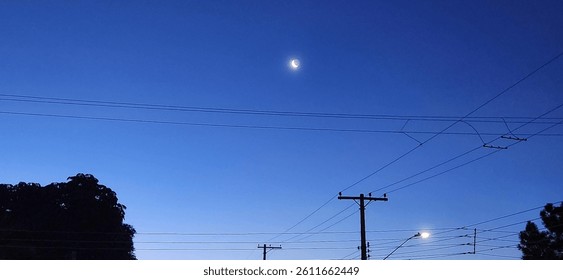 A serene night scene with a deep blue sky adorned by a waning moon. Power lines cut through the image, creating a contrast between nature and urban infrastructure. - Powered by Shutterstock - Get 15% off with code: PIKWIZARD15
