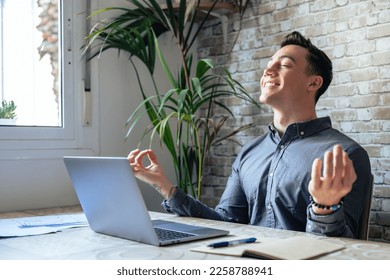 Serene office male employee sit at desk relaxing doing yoga, practice meditation to reduce stress relief fatigue feel internal balance at workplace, improve mindfulness, maintain mental health concept - Powered by Shutterstock