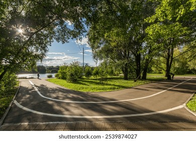 A serene park pathway curved along the riverside with walking inhabitants enjoying nature on a sunny afternoon
 - Powered by Shutterstock