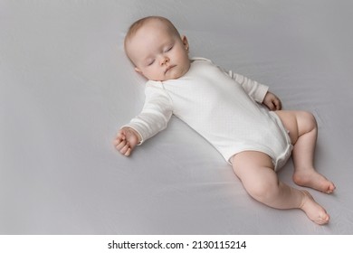 Serene Peaceful Sweet Baby In White Bodysuit Sleeping On Double Bed, Lying Pn Back On Pale Sheet. Few Month Sleepy Infant Child Resting On Soft Mattress. Child Care Daily Routine Concept