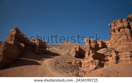 serene photograph showcases the tranquil beauty of a desert canyon with towering red sandstone formations under a vast, clear blue sky, captured on a warm, sunny day