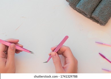 Serene Pink Beauty Background With Lash Artist Products And Tools.  Hands Holding Onto Lash Tweezers In Lower Section Of Frame. Space For Copy Text And Customisation