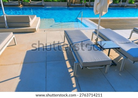 Serene poolside scene featuring modern lounge chairs, umbrellas, and a clear blue swimming pool under bright sunlight, creating a relaxing and luxurious atmosphere