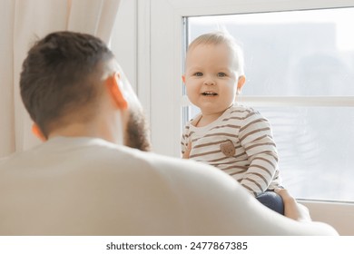 Serene portrait of father baby interaction by window, with dad attentive gaze and little son curious exploration emphasizing familial connection. - Powered by Shutterstock