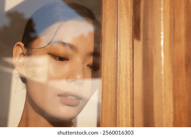 Serene Portrait of a Woman Reflected Through a Sunlit Wooden Frame, Capturing Warm Tones and Tranquil Emotions. - Powered by Shutterstock