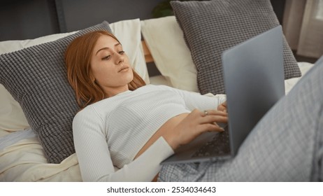 A serene redhead woman relaxes in bed using her laptop in a cozy bedroom setting. - Powered by Shutterstock