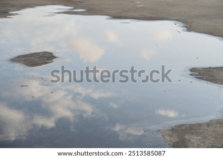 A serene reflection of clouds in a puddle on a concrete surface, showcasing a tranquil moment in nature.
