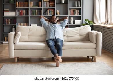 Serene relaxed barefoot young african man resting on comfortable couch in modern living room holding hands behind head, millennial hipster guy enjoy no stress peace of mind lounge on sofa at home - Shutterstock ID 1626375400