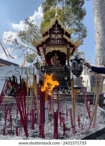 The serene ritual of burning incense sticks in front of a traditional Thai spirit house, a practice steeped in culture and spirituality.