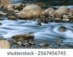 A serene river flowing over smooth rocks. The water appears silky due to long exposure, creating a tranquil scene. Wulai District, New Taipei City, Taiwan.