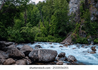 A serene river flowing through a lush green forest with rocky banks and a backdrop of tall trees and cliffs. - Powered by Shutterstock