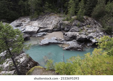 A serene river flowing through rocky terrain surrounded by lush green trees. - Powered by Shutterstock