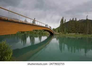 Serene river, framed by the shadow of mountains and trees, flows gently under an ancient stone bridge. Nature's quiet embrace is reflected in its tranquil waters, weaving a picturesque scene of peace - Powered by Shutterstock