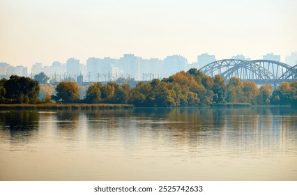 A serene riverscape with autumnal trees reflected in the water, a bridge in the distance, and a hazy city skyline. The calm atmosphere evokes the transition between nature and urban life. - Powered by Shutterstock