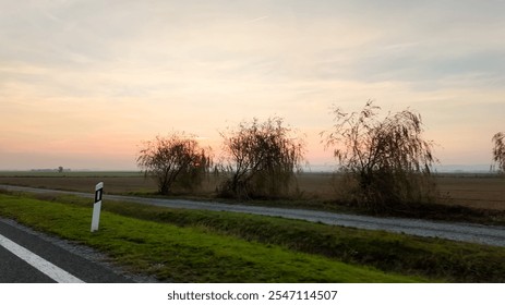 A serene rural landscape with a sunset behind bare trees along a country road, evoking tranquility and introspection - Powered by Shutterstock