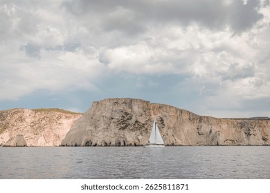 A serene sailboat navigates calm waters near impressive cliffs, with dramatic clouds overhead. The peaceful atmosphere invites moments of reflection and adventure at sea - Powered by Shutterstock - Get 15% off with code: PIKWIZARD15