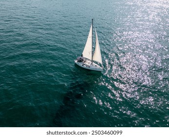 A serene sailing boat glides on calm, deep blue waters under a clear sky. Distant ships and sailboats dot the horizon, creating a peaceful maritime scene - Powered by Shutterstock