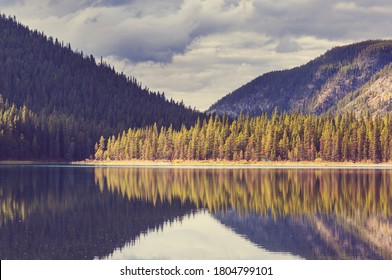 Serene Scene By The Mountain Lake In Canada With Reflection Of The Rocks In The Calm Water.