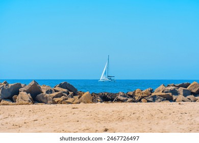 Serene scene at Venice Beach featuring a sandy shoreline, scattered boulders, a tranquil ocean, and a sailboat in the distance. - Powered by Shutterstock