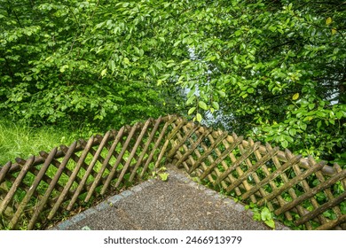 Serene scene of weathered wooden fence, lush green foliage and gravel ground in natures embrace. - Powered by Shutterstock