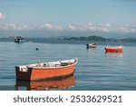 A serene seascape featuring small boats floating on calm water with distant mountains and a clear blue sky.