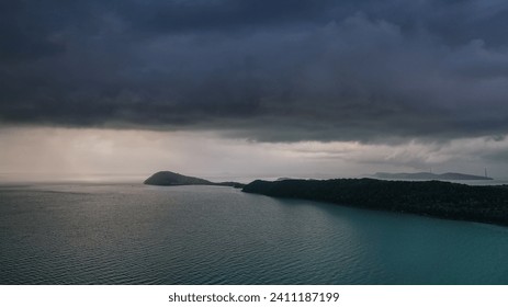 A serene seascape with overcast skies signaling an approaching storm over tranquil waters, featuring islands and a forested coastline - Powered by Shutterstock