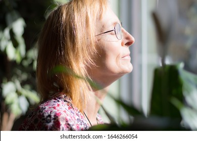 Serene Senior Woman With Closed Eyes Enjoys Outside Sun Through Window. Older Woman With Glasses