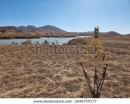 A serene setting with a lone tripod standing tall in a vast field next to the shimmering lake in the large desert, inviting exploration and creativity