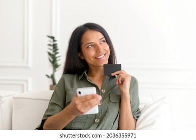 Serene Smiling Dreamy Indian Woman Holding Credit Card And Smartphone, Thinking About Long Awaited Purchase, Happy Inspired Eastern Lady Is Shopping Online, Paying For Travel Voucher, Booking Online