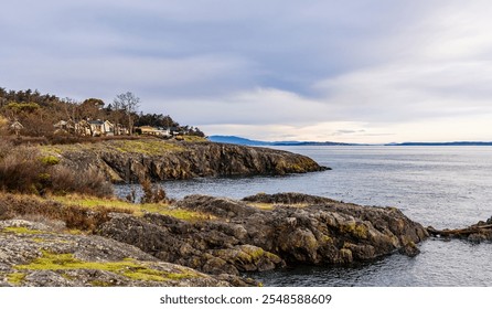 Serene sunrise scene in Victoria, Vancouver Island, showcasing a rocky coastline with houses nestled among trees by the water. The tranquil atmosphere evokes calmness and natural beauty. - Powered by Shutterstock