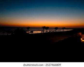 A serene sunset over the calm sea, with vibrant hues of orange and blue. Silhouetted palm trees line the shore, creating a peaceful atmosphere perfect for relaxation. - Powered by Shutterstock