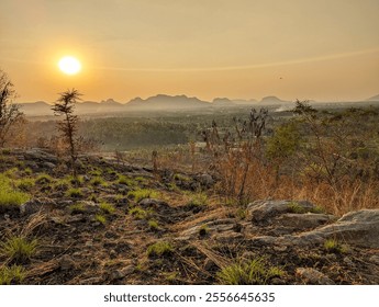 Serene sunset over a rural countryside with mountains, lush green fields, scattered trees, rocky terrain. Warm golden hues create a tranquil, scenic landscape, perfect for nature and rustic beauty. - Powered by Shutterstock