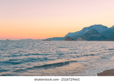 A serene sunset over the tranquil beach with distant ships on the horizon near coastal mountains - Powered by Shutterstock