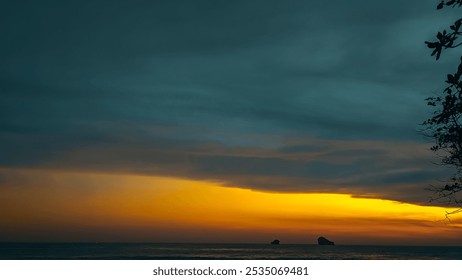 A serene sunset paints the sky in hues of orange and gold, casting a warm glow over the calm ocean. Silhouetted against the twilight sky, a lone tree stands tall on the shore, its branches reaching ou - Powered by Shutterstock