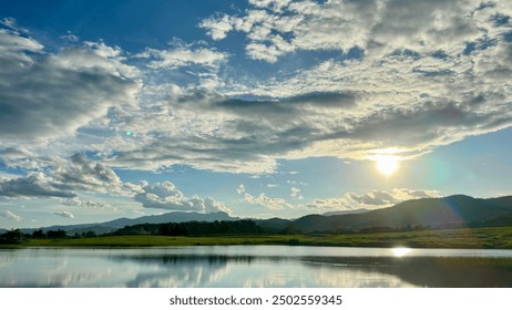 Serene Sunset Reflection: A tranquil scene of a serene lake reflecting the golden hues of a setting sun, with lush green grass and distant mountains, evoking a sense of peace and tranquility.   - Powered by Shutterstock