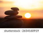 Serene sunset with a stack of balanced stones silhouetted against a vibrant sky, symbolizing tranquility, harmony, and mindful reflection in nature