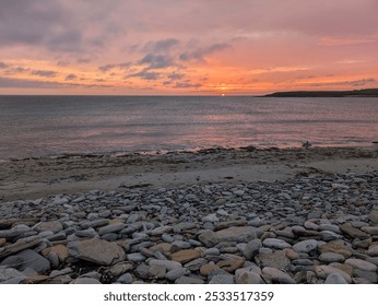 A serene sunset view over a rocky beach with a calm sea and colorful sky. - Powered by Shutterstock