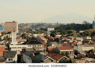 Serene sunset view over Semarang, with the city's architecture nestled amidst lush greenery and a distant mountain range. - Powered by Shutterstock