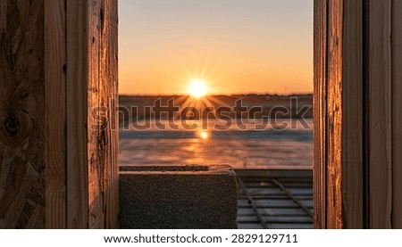 A serene sunset viewed through a rustic wooden frame, casting a warm glow over tranquil water and distant landscape.