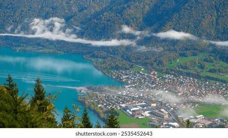 A Serene Swiss Alpine Village Grindelwald on the lake Brienz in Early Autumn, Nestled Amid Lush Green Meadows and Hills Covered with Pine Forests, Beneath a Blanket of Mist and Low-Hanging Clouds - Powered by Shutterstock