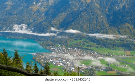 A Serene Swiss Alpine Village Grindelwald on the lake Brienz in Early Autumn, Nestled Amid Lush Green Meadows and Hills Covered with Pine Forests, Beneath a Blanket of Mist and Low-Hanging Clouds - Powered by Shutterstock