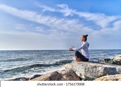 Serene ruhige Frau in Lotus Position meditiert und entspannt auf einer Klippe auf dem Hintergrund des Meeres und des blauen Himmels. Calm Konzept und Gleichgewicht der psychischen Gesundheit             