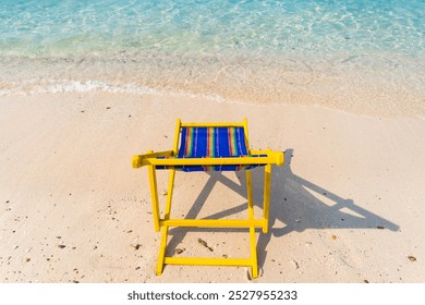 A serene tropical beach scene featuring a vibrant yellow and blue beach chair on pristine white sand, overlooking clear turquoise waters and lush green hills under a clear blue sky. - Powered by Shutterstock