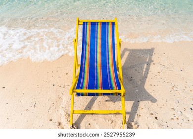 A serene tropical beach scene featuring a vibrant yellow and blue beach chair on pristine white sand, overlooking clear turquoise waters and lush green hills under a clear blue sky. - Powered by Shutterstock