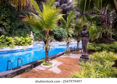 A serene tropical poolside surrounded by lush greenery, palm trees, and a stone Buddha statue, evoking tranquility and natural beauty - Powered by Shutterstock